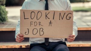 Das Bild zeigt einen Mann, der einen Karton vor sich hält, auf dem steht: "Looking for a job".